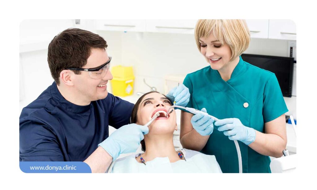 تصویر دندانچزشک و دستیارش در حال ترمیم دندان بیمار